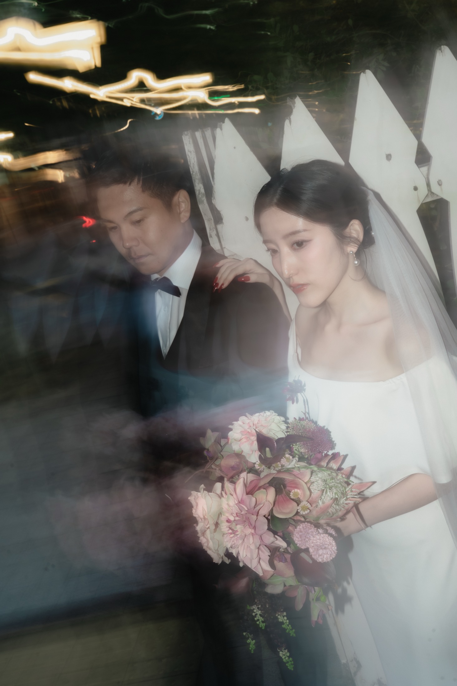 夜の街で、白いドレスにベールをまとい、ブーケを手にした花嫁とタキシードの花婿